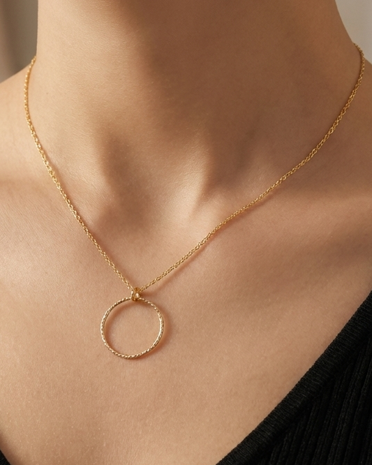 Gold necklace with a circular pendant worn by a person in a black top.