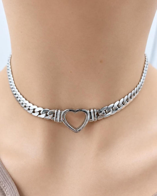 A silver-toned metal choker necklace with a heart-shaped center clasp, shown worn on a model's neck.