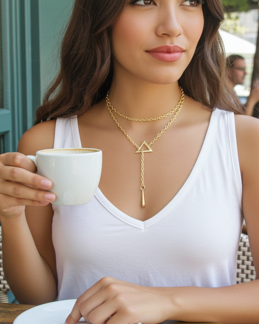 Woman holding a cup of coffee wearing a gold necklace with a triangle pendant.