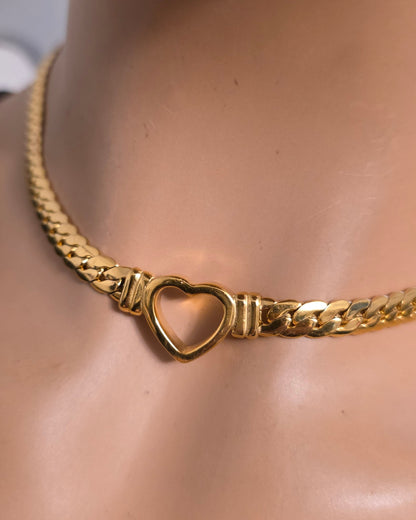 A gold chain choker necklace with a heart-shaped clasp, displayed on a mannequin bust wearing a black top.