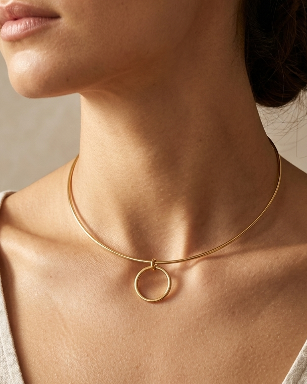 Close-up of a woman wearing a gold necklace with a circular pendant against a neutral background.