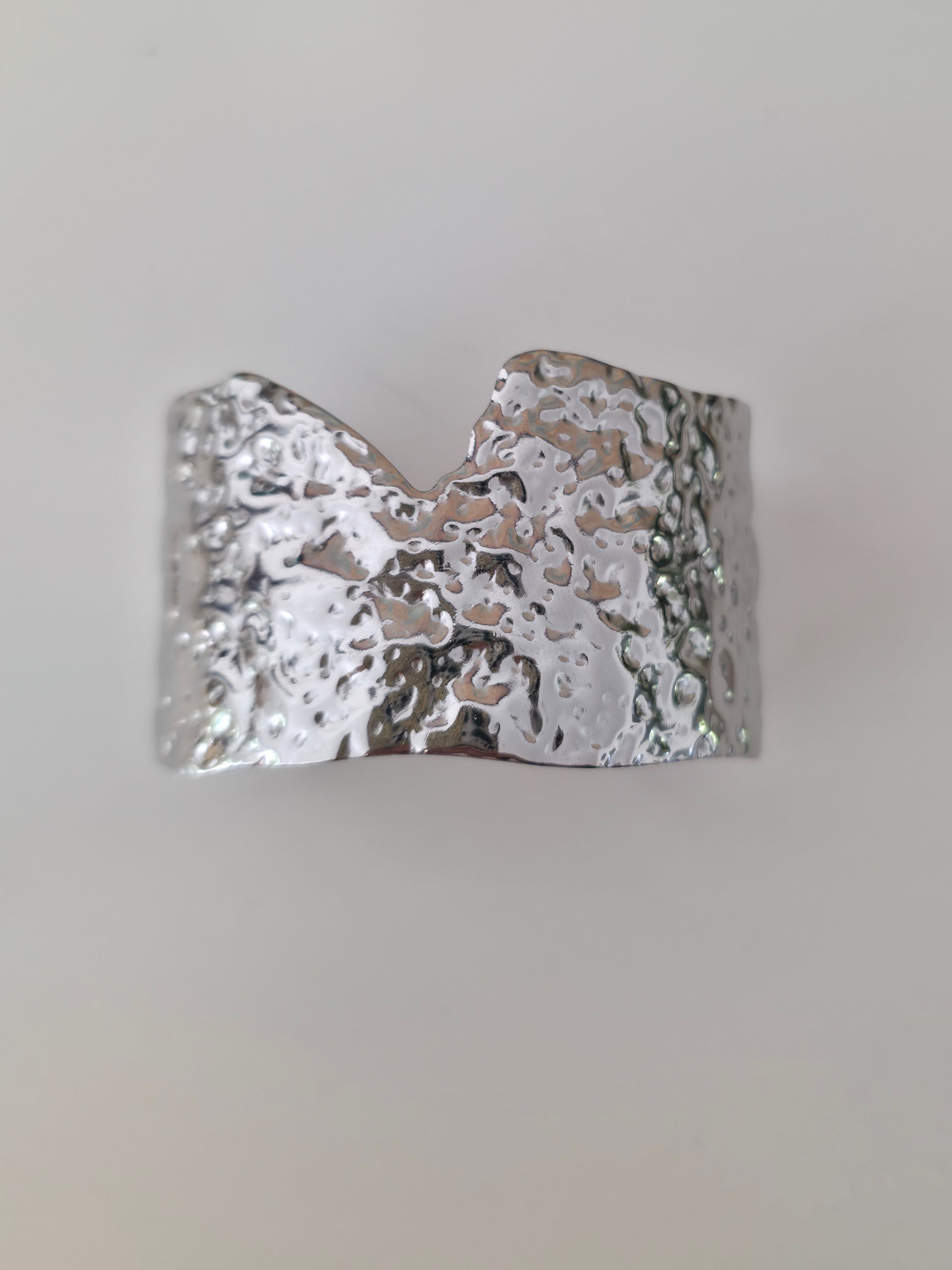 Silver cuff bracelet with textured surface on a light gray background