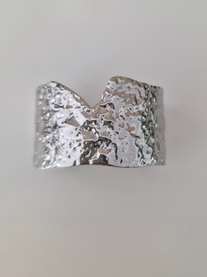 Silver cuff bracelet with textured surface on a light gray background