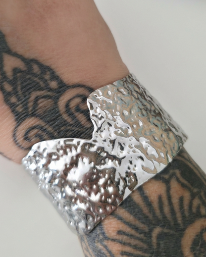 Silver textured cuff on a wrist with tattoos