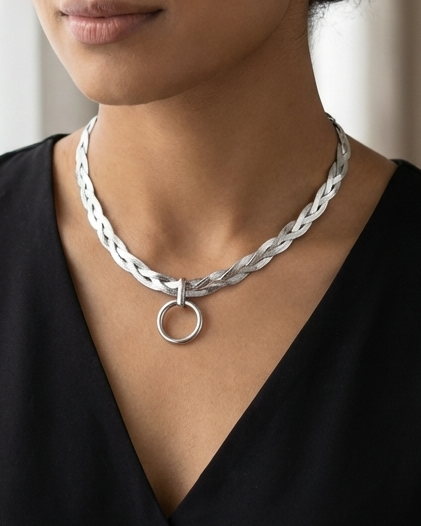 Woman wearing a silver braided necklace with a circular pendant against a neutral background