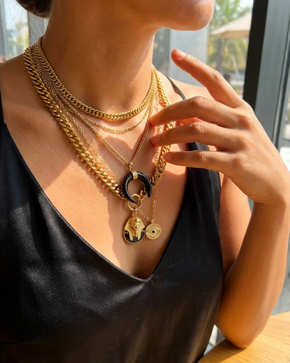 Person wearing multiple gold necklaces with a blurred outdoor background