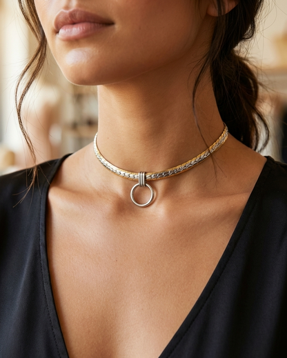 A close-up of a woman wearing a silver-toned chain choker necklace with a circular ring pendant, paired with a black V-neck top.