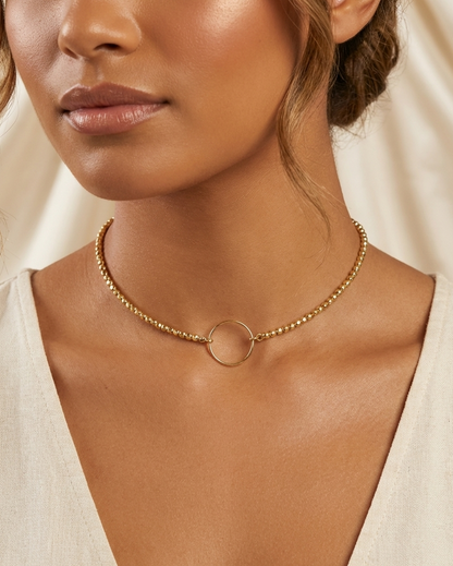 Close-up of a woman wearing a gold necklace with a plain background