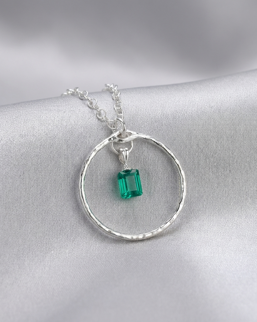 Silver necklace with a green gemstone pendant on a gray background