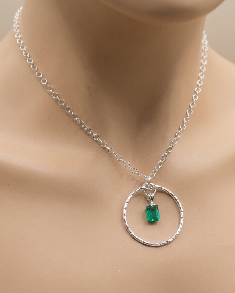 Silver necklace with a green gemstone pendant on a mannequin.