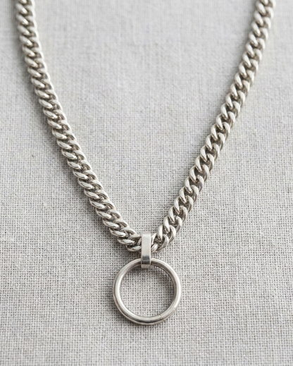 Silver chain necklace with a round pendant on a light gray background