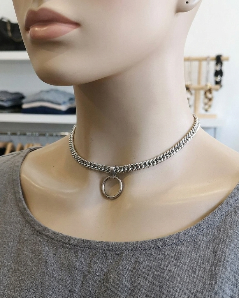 Mannequin wearing a silver chain necklace with a circular pendant in a store setting.