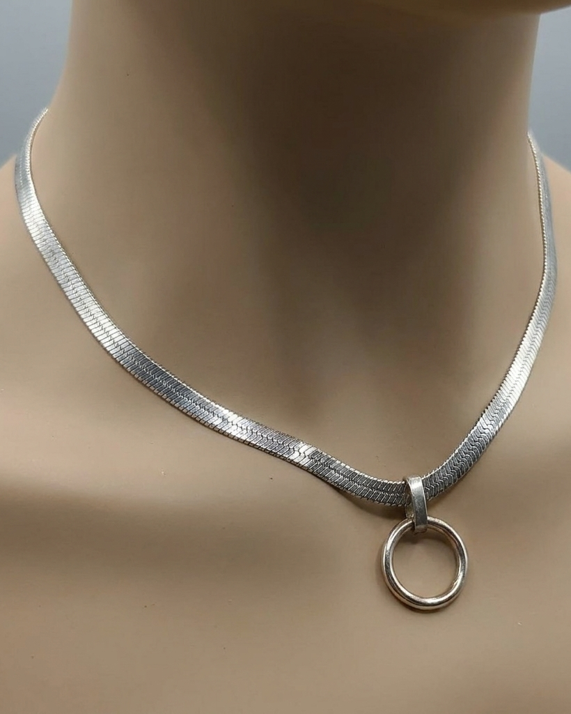 Silver necklace with a circular pendant on a mannequin neck against a neutral background