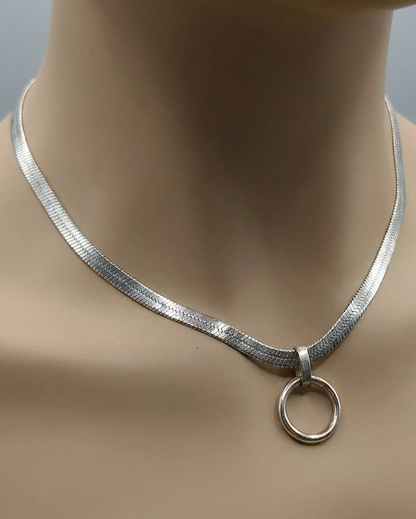 Silver necklace with a circular pendant on a mannequin neck against a neutral background