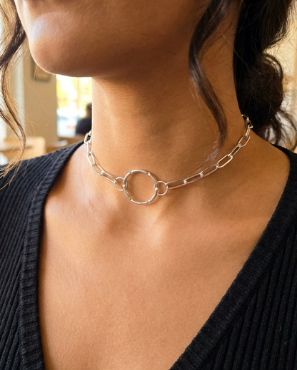 Close-up of a person wearing a silver chain necklace with blurred indoor background