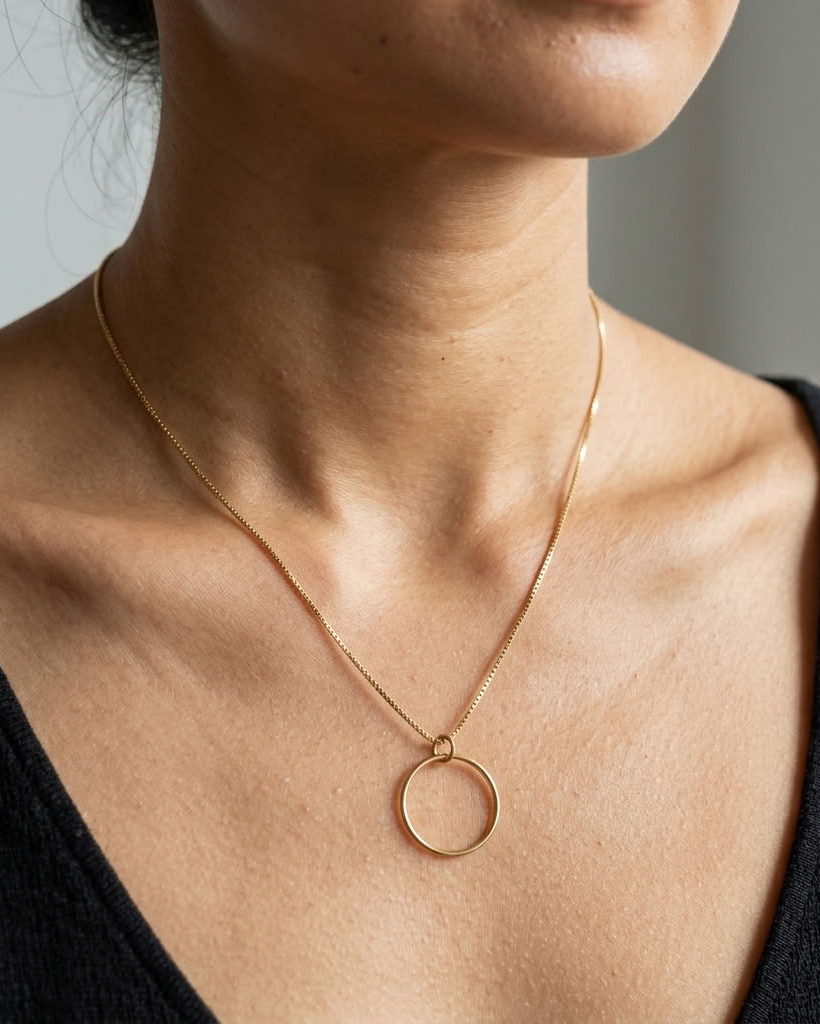 A close-up of a model wearing a delicate gold chain necklace with a thin circular pendant, styled with a black top.