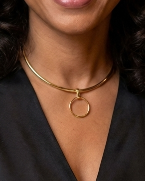 Woman wearing a black top and gold necklace with a blurred background