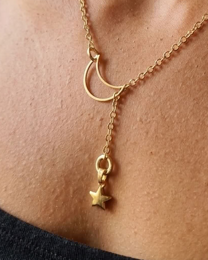 A close-up lifestyle shot of a model wearing a delicate gold necklace with a crescent moon and star pendant layered over a shorter chain.