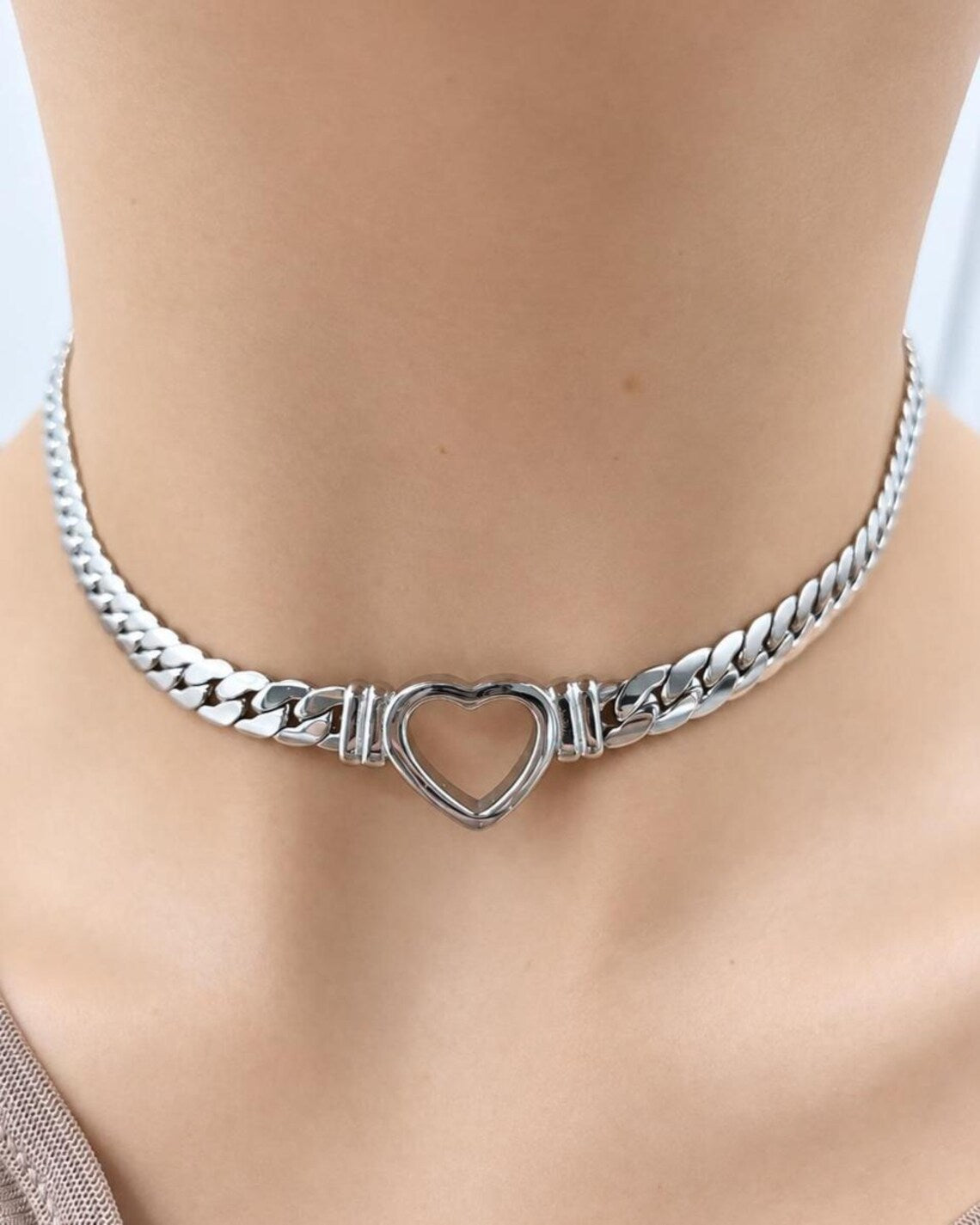 A silver-toned metal choker necklace with a heart-shaped center clasp, shown worn on a model's neck.