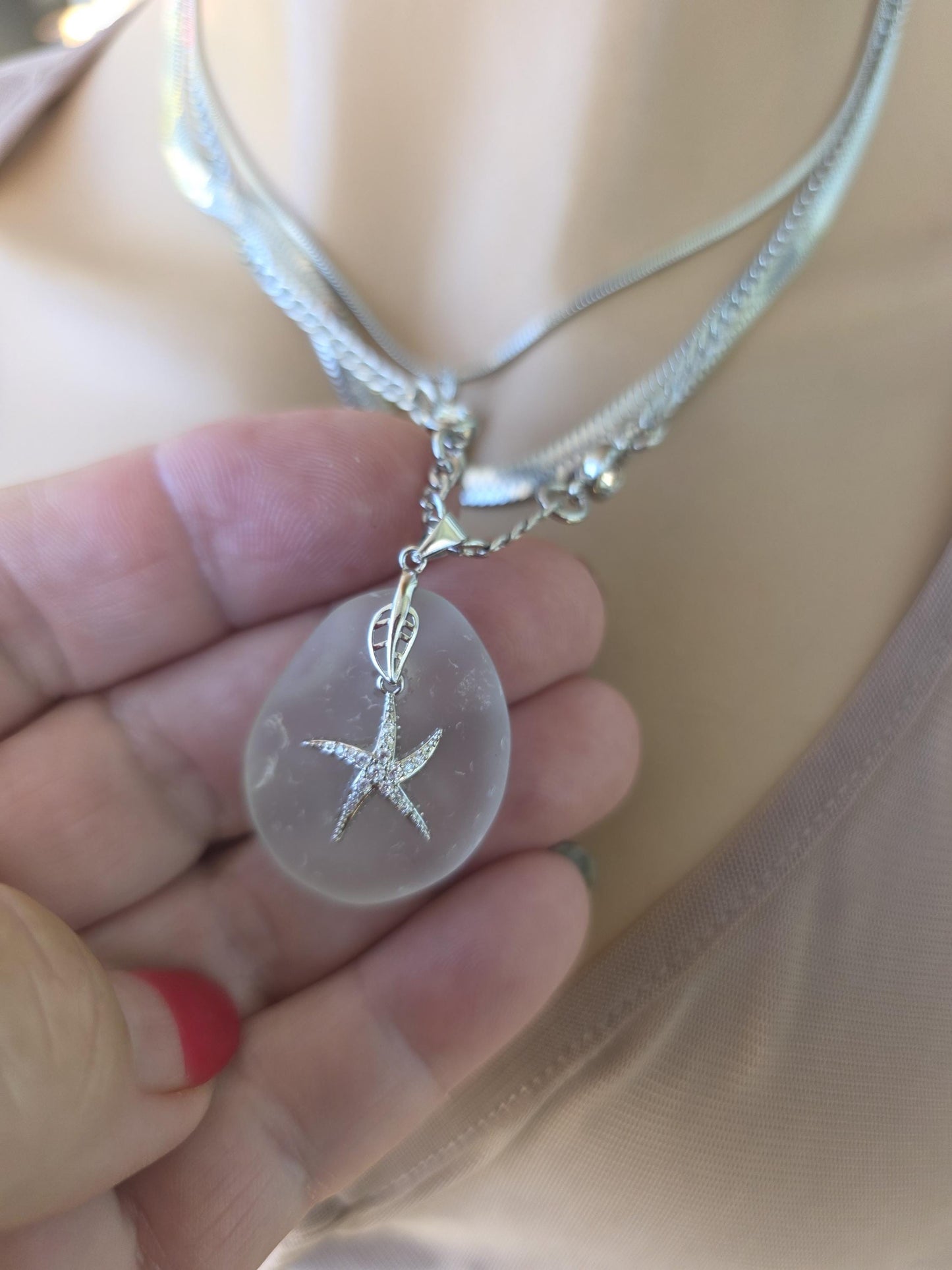 Photo of a genuine ocean-tumbled sea glass pendant in stainless steel bezel on a stainless steel chain, handmade coastal jewelry inspired by Norse goddess style.