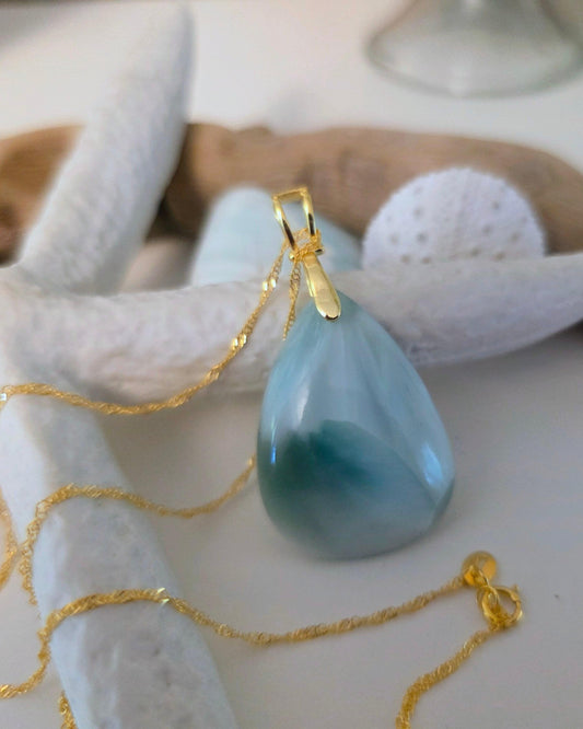 Blue teardrop pendant on a gold chain with starfish and shells in the background