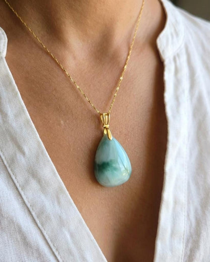 Necklace with a green teardrop pendant worn by a person in a white shirt.