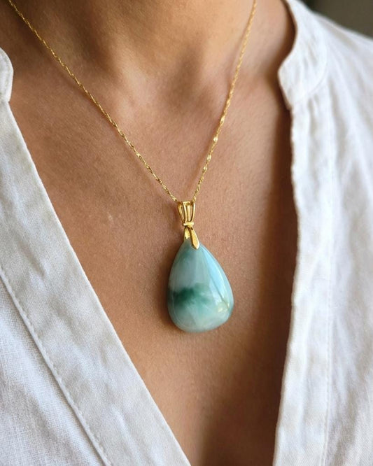 Necklace with a green teardrop pendant worn by a person in a white shirt.