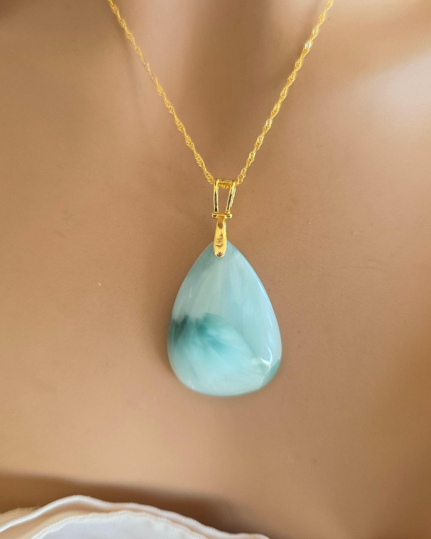 Gold necklace with a teardrop-shaped light blue pendant on a mannequin.