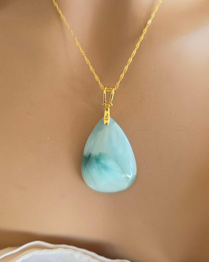 Gold necklace with a teardrop-shaped light blue pendant on a mannequin.