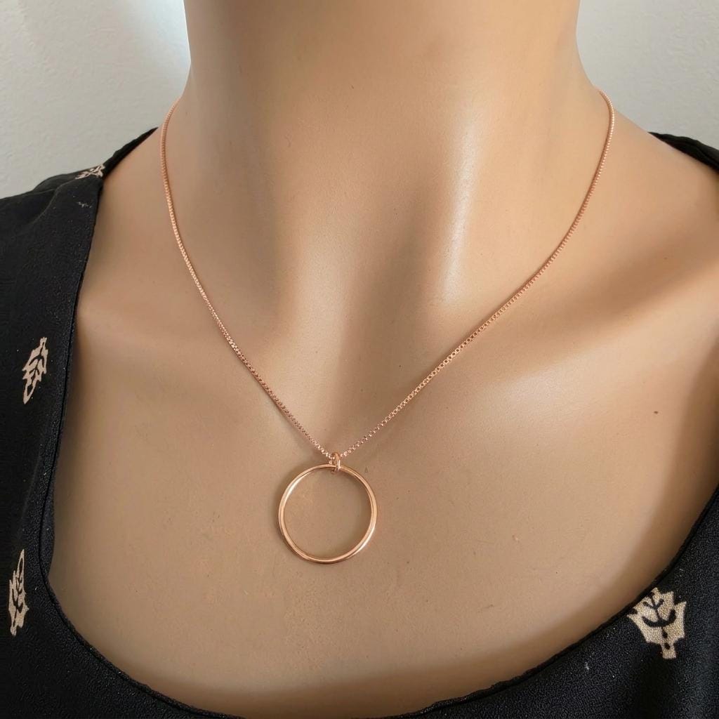 May include: A rose gold necklace featuring a delicate box chain and a simple, circular pendant. The metal has a warm, metallic finish, and the circular charm hangs centered from the thin chain, creating a clean and understated jewelry piece.