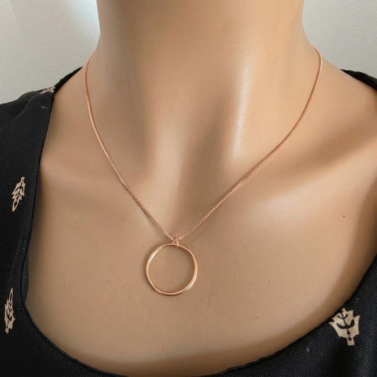 May include: A rose gold necklace featuring a delicate box chain and a simple, circular pendant. The metal has a warm, metallic finish, and the circular charm hangs centered from the thin chain, creating a clean and understated jewelry piece.