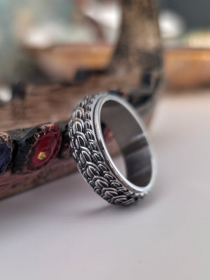 Silver ring with intricate design on a reflective surface