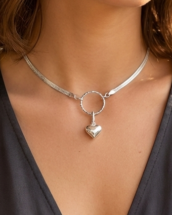 Woman wearing a silver necklace with a heart pendant against a blurred natural background