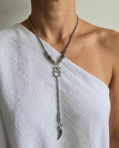 Person wearing a silver necklace with star and feather pendant on a plain background